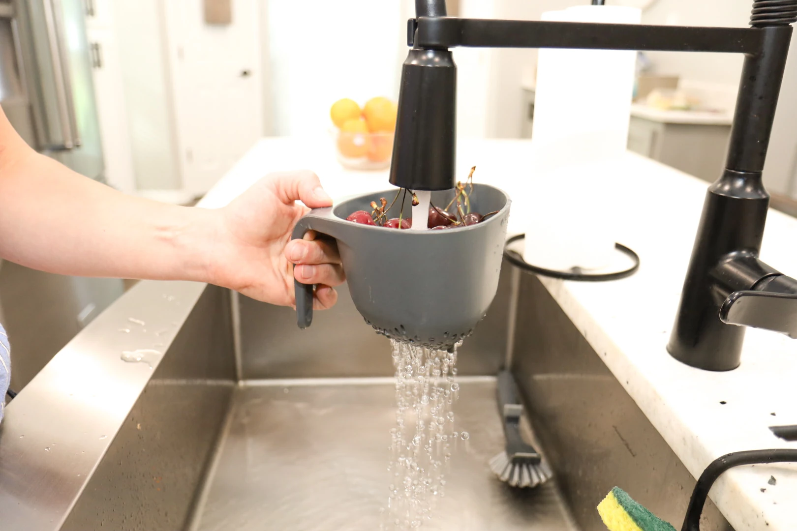 A mom rinsing off a colander of fruit under a running sink faucet.