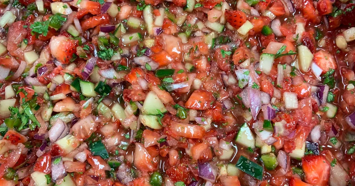 Close-up on a strawberry salsa consisting of coarsely diced strawberries, red onion, cilantro, and cucumbers.
